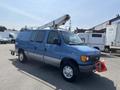 A blue 2005 Ford Econoline van with a raised bucket lift mounted on top and a red flag attached to the front bumper