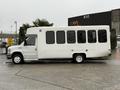 A white 2017 Ford E450 shuttle bus with large windows parked on a paved surface