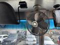 A metal fan mounted on the ceiling of a vehicle with a black clamp attached to the side