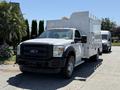 A white 2013 Ford F-550 truck with an aluminum utility box and orange roof lights parked with another vehicle behind it