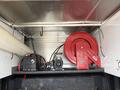 A red air compressor mounted on a metal surface with a black battery nearby and hoses connected to the compressor
