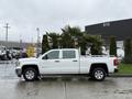 A 2015 GMC Sierra 1500 pickup truck in white with a crew cab parked parallel to a palm tree on a wet surface