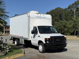 A 2013 Ford Econoline box truck with a white exterior and a ladder rack on top parked at an angle with its front facing the viewer