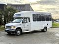 A white 2002 Ford Econoline bus with large windows and a boxy shape is parked at an angle showcasing its front and side profile