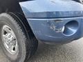 A blue 2006 Dodge Ram 2500 with a damaged front bumper and a shiny chrome wheel, showcasing scuffs and scratches on the bumper surface