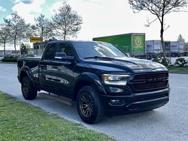 A black 2019 RAM 1500 truck with chrome accents and off-road tires parked on a pavement with a shiny surface and a prominent front grille