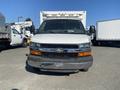 A white 2011 Chevrolet Express van with a black grille and orange accents positioned in front of other vehicles