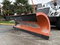 A large orange snow plow blade attached to a truck, featuring a black trim and markings on the surface