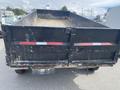 A black 2014 PJ 16 foot dump trailer with a metal body and gravel in the bed featuring two red and white reflective stripes on the rear panel