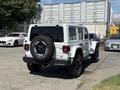 A 2021 Jeep Wrangler in white with black accents parked with a spare tire mounted on the rear and off-road tires on the wheels