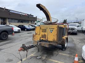 A yellow 2015 Vermeer Corporation BC1200XL wood chipper with a chute on top and a wheeled trailer hitch in the back