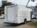 A 2018 Ford Econoline van with a boxy cargo area and a rear roll-up door parked with a ladder extending from the roof