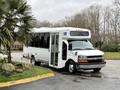 A 2013 Chevrolet Express bus with an accessible entrance and large front windows is parked with its door open showing a spacious interior