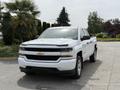 A white 2018 Chevrolet Silverado 1500 pickup truck is parked with a prominent front view showcasing its chrome grille and headlights