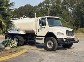 A white 2016 Freightliner M2 106 truck with a large tank on the back, designed for transporting liquids, parked and facing slightly to the right