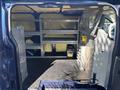 The interior of a 2016 Ford Transit 150 van featuring shelving units on both sides a partition and storage compartments for tools and equipment