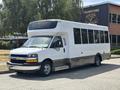 A 2020 Chevrolet Express van with a white exterior and large windows is parked on a pavement. It has a low step and a distinctive front grille design