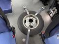 A spare tire secured with straps on the floor of a vehicle, surrounded by two blue upholstered seats
