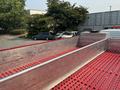 A 1999 Freightliner FL80 flatbed truck with a metallic frame and red perforated flooring has a long, empty cargo area