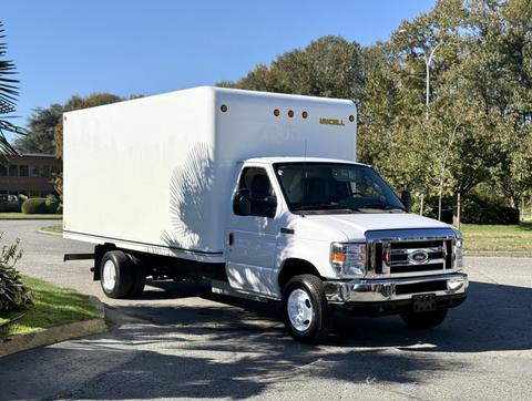 A white 2019 Ford E-450 box truck with six circular lights on top and a flatbed chassis facing slightly to the right