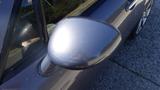 A 2007 Mazda Miata with a shiny silver side mirror reflecting light and details from nearby objects