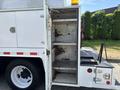 A white 2006 International 4300 truck with an open compartment revealing three empty metal shelves and a small light on top