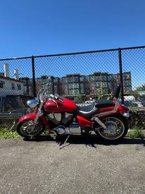 A red 2007 Honda VTX1800F3 motorcycle with chrome accents and a low seat positioned on a gravel surface