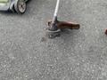 Three Honda Lawnboy mowers and two Stihl line trimmers arranged on a surface with one trimmer in focus showcasing its cutting head and spool mechanism