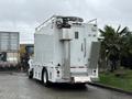 A white 2011 Ford F-650 with a boxy body design features side access doors and a rooftop structure with various equipment attached