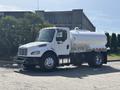A white 2014 Freightliner M2 106 truck with a cylindrical tank attached to the back and shiny chrome wheels parked on a street