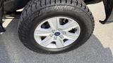 A close-up of a silver alloy wheel with the Ford logo and a rugged tire tread on a 2016 Ford F-150