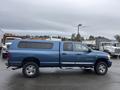 A blue 2006 Dodge Ram 2500 with a camper shell parked at a lot the truck has chrome wheels and a side step bar