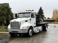 A 2020 Peterbilt 330 truck with a white cab and a flatbed chassis parked on a wet surface with orange cones nearby