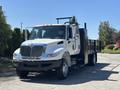 A 2011 International 4300 truck with a flatbed and a black railing on the back, featuring a white cab and large front grille with headlights