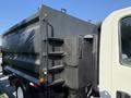 A 2017 Isuzu NPR HD truck with a dark black dump body featuring side storage compartments and a ladder on the back