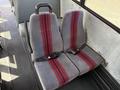 Two gray bus seats with red stripes and seatbelts arranged side by side on a bus interior floor