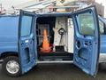 A blue 2006 Ford Econoline van with open double doors revealing interior equipment including a traffic cone and various tools and machinery