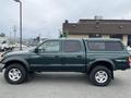 A green 2004 Toyota Tacoma pickup truck with a bed cap is parked, featuring four doors and alloy wheels