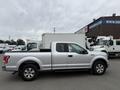 A silver 2015 Ford F-150 pickup truck with a flatbed and extended cab parked on a street