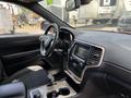 Interior view of a 2015 Jeep Grand Cherokee featuring a black dashboard leather-wrapped steering wheel and infotainment system with climate controls and center console storage