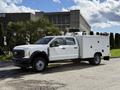 A 2024 Ford F-550 truck with a white exterior features a utility box on the rear and is parked with visible wheels and side mirrors