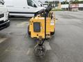 A yellow 2014 Vermeer Corporation Sweep Stump Cutter with large wheels and a cutting blade at the front positioned on a pavement surface