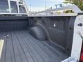 A white 2021 Ford F-250 SD truck bed showing a clean, textured surface with a molded wheel well and side attachments for securing cargo