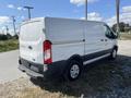 A white 2017 Ford Transit van parked on the side of the road featuring sliding side doors and a rear cargo area