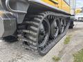A yellow 2004 Bombardier SW48 snow groomer with large rubber tracks featuring deep treads for traction and three visible drive wheels