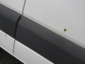 A 2009 Dodge Sprinter Van with rust spots on the side panel and a smooth gray lower section