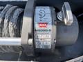 A WARN MB8000-S winch with a coiled steel cable and instruction labels on a metal housing