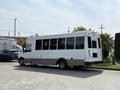 A white 2020 Chevrolet Express shuttle bus with black trimming and large windows parked on a gravel surface