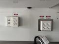 A wall with electrical outlets labeled with danger signs indicating 115 volts and a mounted inverter with additional socket outlets