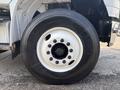 A close-up of a large black tire mounted on a white rim with visible lug nuts and tire brand lettering on the sidewall